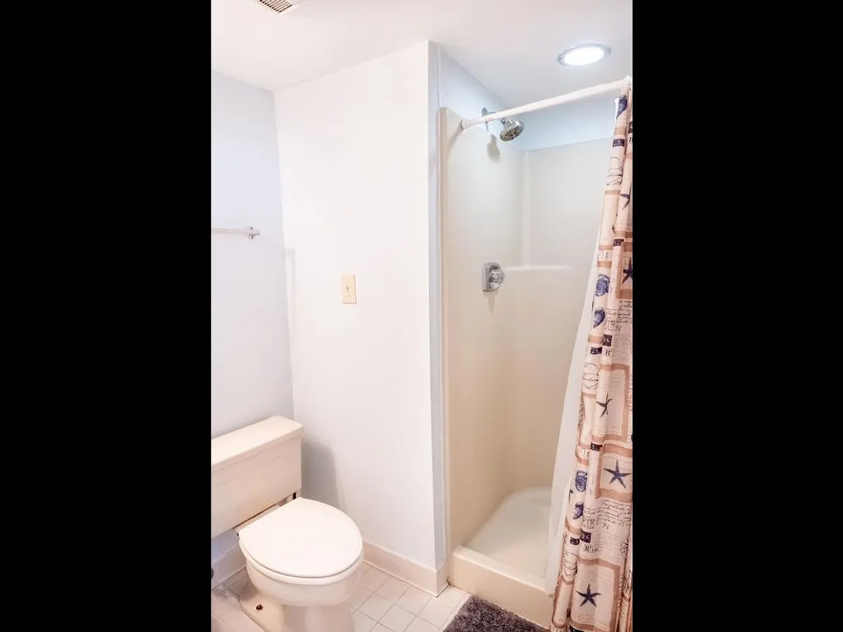 A modern bathroom with a shower, shower curtain, and toilet. The serene palette and practical layout provide a sense of everyday luxury and privacy, perfect for post-beach relaxation.