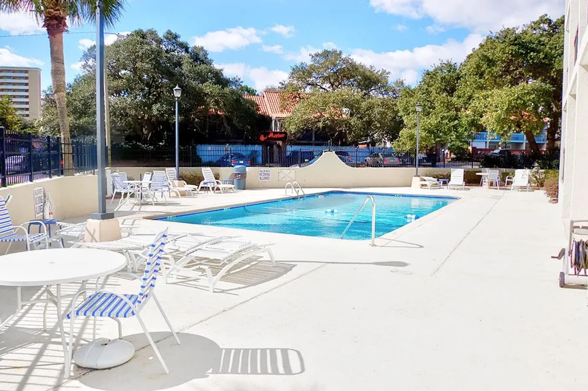 The hero image showcases a sparkling outdoor swimming pool surrounded by inviting lounge chairs and outdoor tables, all set amidst swaying palm trees. The scene is bathed in cheerful sunlight, creating a welcoming atmosphere perfect for sunbathing, socializing, and relaxing in the warm Myrtle Beach air.