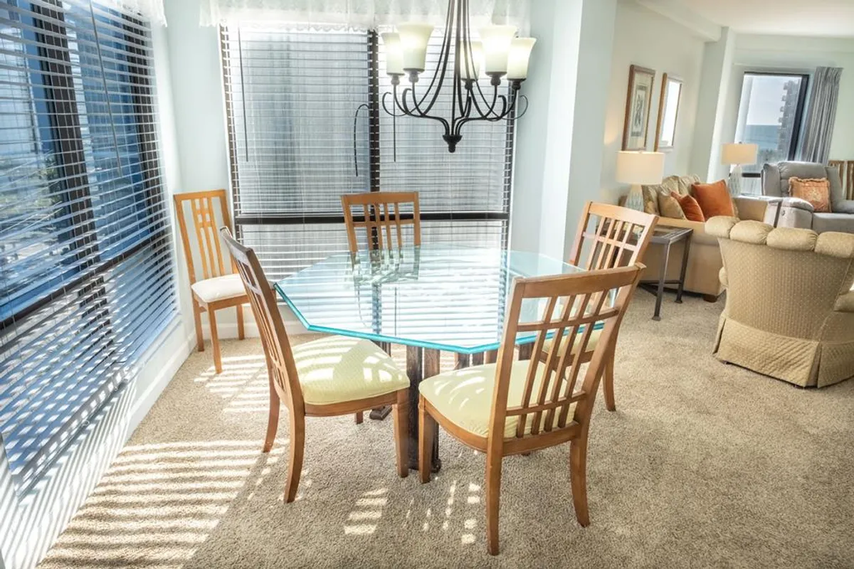 A welcoming dining area featuring a glass dining table illuminated by a stylish chandelier. Wooden chairs surround the table, creating a cozy setting ideal for family meals and shared moments. The overall ambiance is warm and comfortable, perfect for gatherings and celebrations.