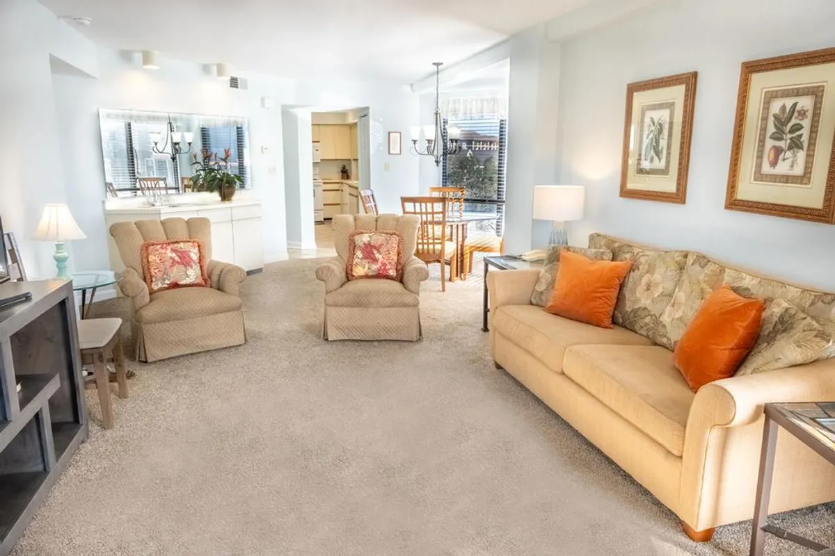 This image displays a bright interior with a sofa, armchairs, a dining table, and a prominent light fixture. Soft morning light filters through the space, providing an inviting and comfortable atmosphere that immediately feels welcoming upon entry. The arrangement of furniture hints at social spaces perfect for families and guests to settle in and relax after arrival.