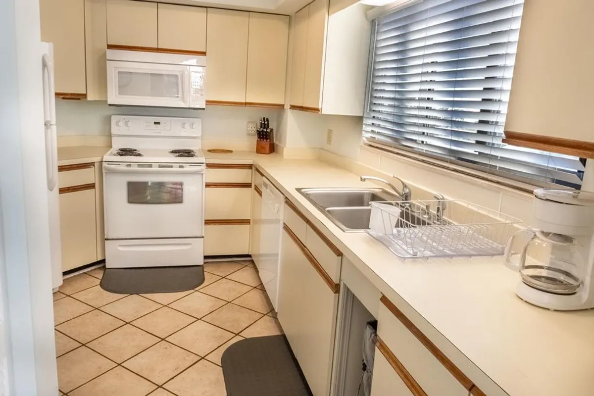 A bright, practical kitchen showcasing a white stove, spacious countertop, and a window that fills the room with natural light. The layout is ready for both meal prep and socializing, inviting guests to participate in cooking and conversation.